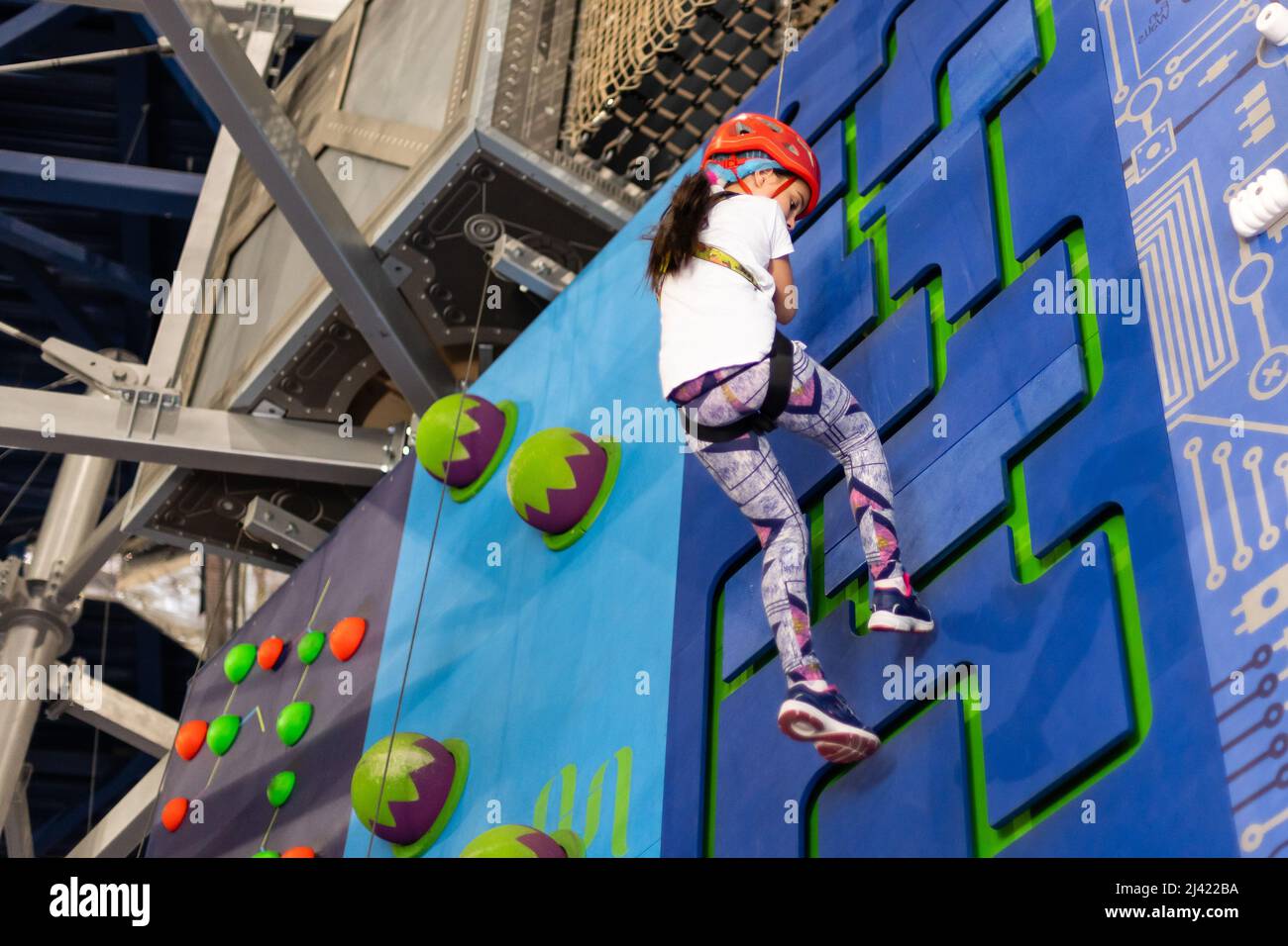 Girl wearing in harness and safety equipment climbing on practical wall  indoor. Girl inserting the rope in a quickdraw Stock Photo - Alamy