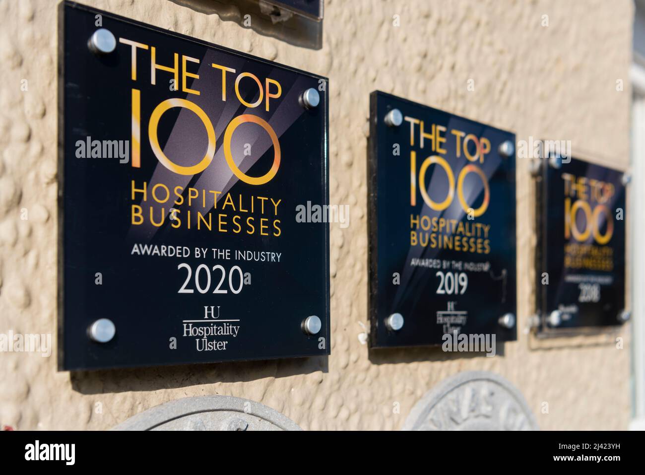 Awards for the Top 100 Hospitality Businesses from Hospitality Ulster for 2018, 2019 and 2020 on the wall outside a restaurant Stock Photo