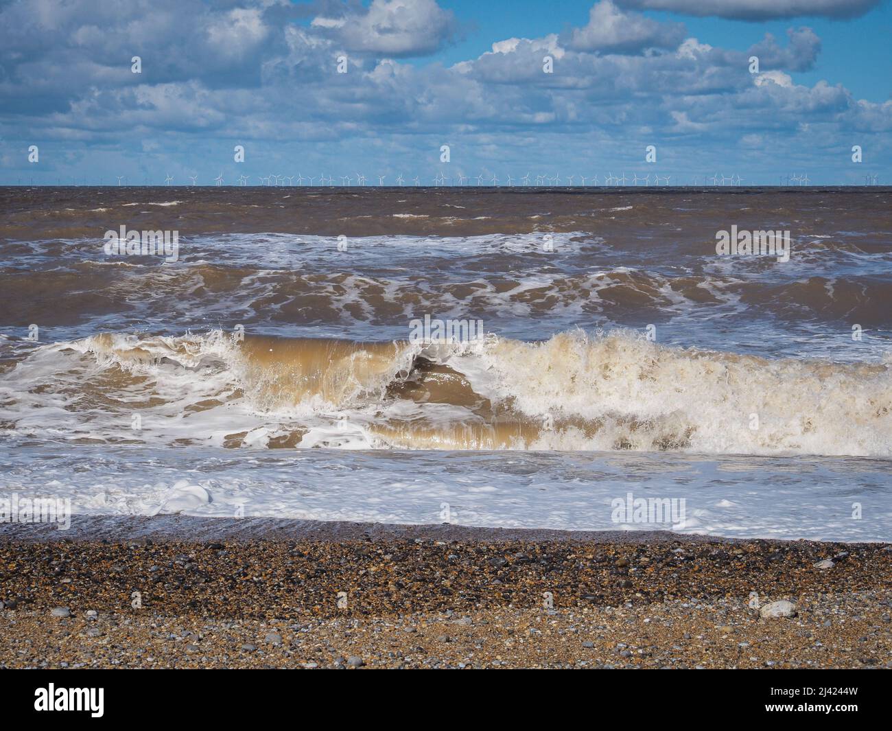 Waves crash onto beach with wind farm on the horizon, Blakeney Point, Norfolk Stock Photo
