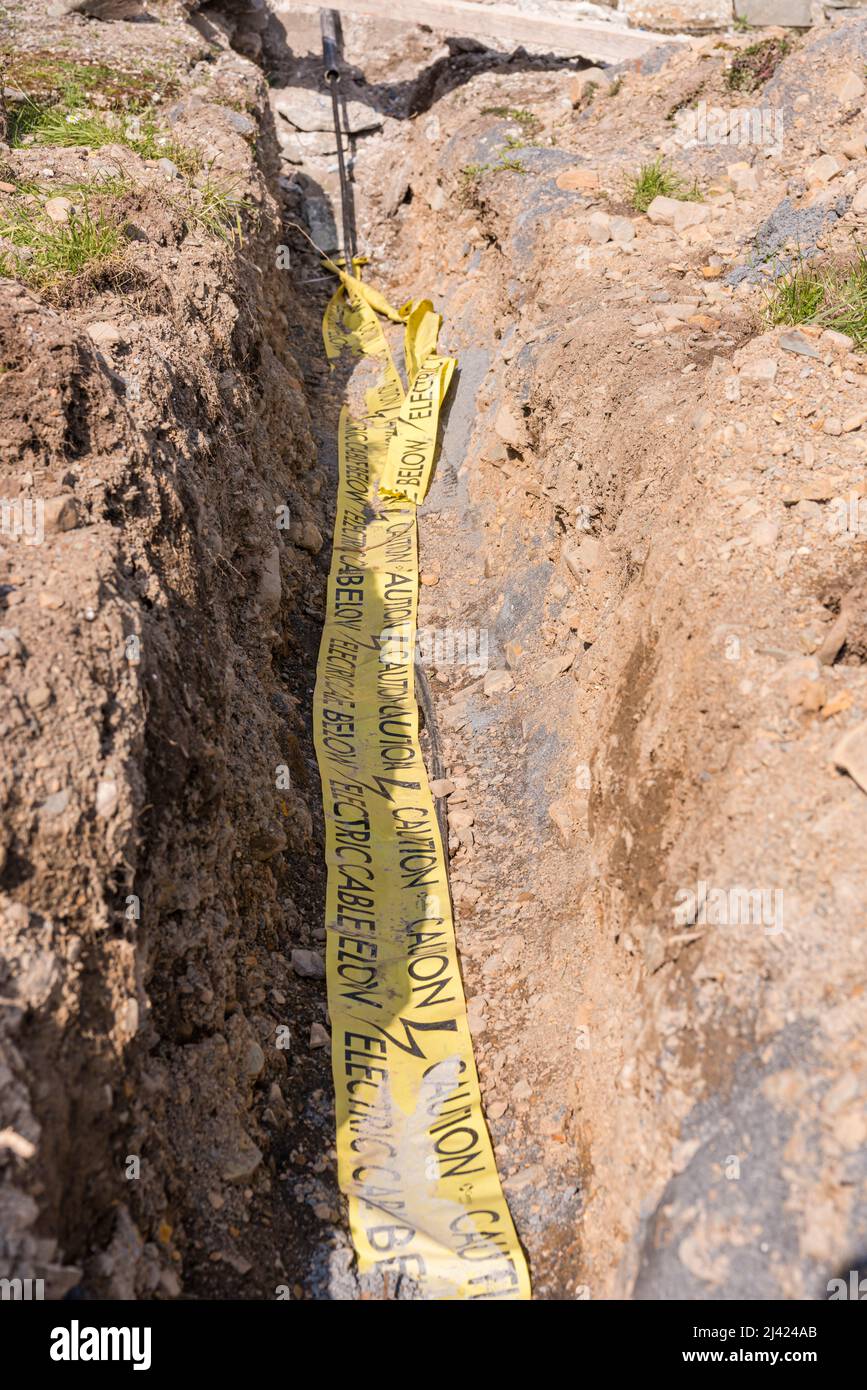 Yellow caution warning tape covering an electrical cable in a trench
