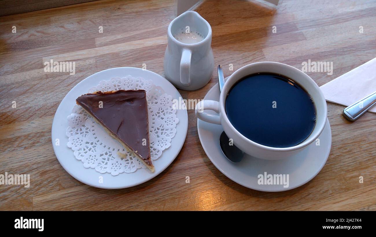 LYTHAM. LANCASHIRE. ENGLAND. 02-27-22. a slice of chocolate topped shortbread served with a cup of black coffee and a small jug of hot milk. Stock Photo