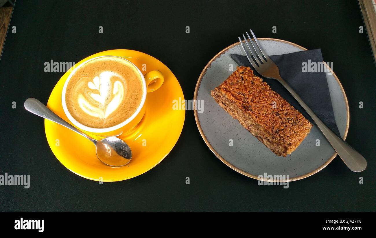 CHESTER; CHESHIRE; ENGLAND; 03-27-22. A cup of coffee in a yellow cup alongside a slice of flapjack cake. Stock Photo