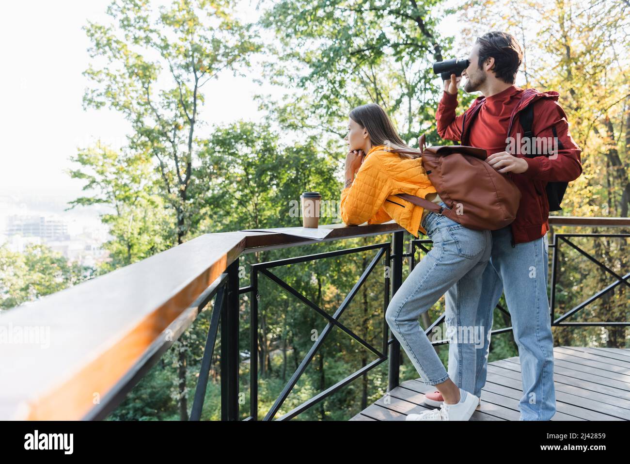 Side view of traveler looking through binoculars near girlfriend, map