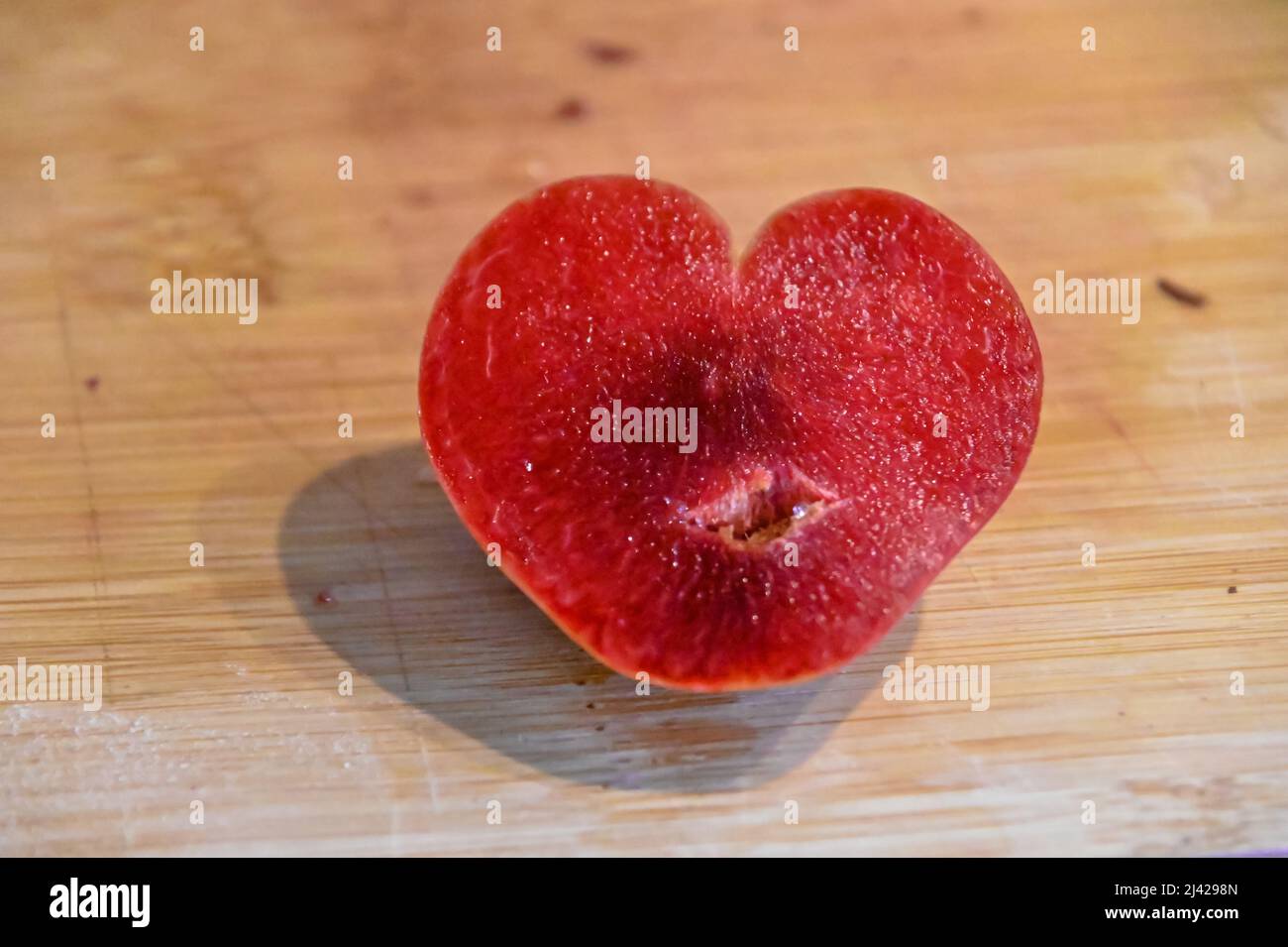 Half of a luscious plum, Prunus subg, naturally shaped in a heart with deep red flesh. Stock Photo