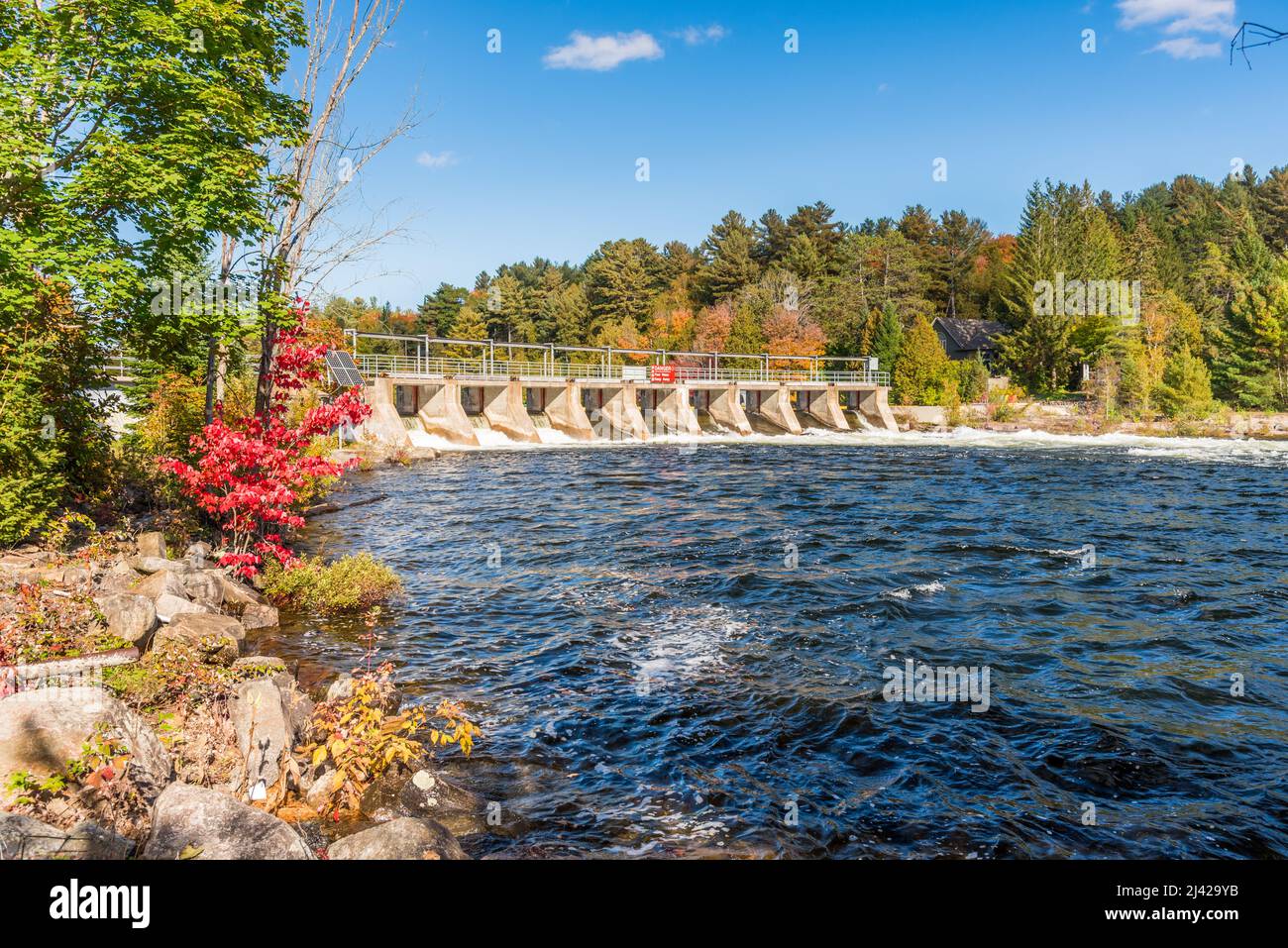 View of a small dam on a river with forested banks on a sunny autumn day Stock Photo