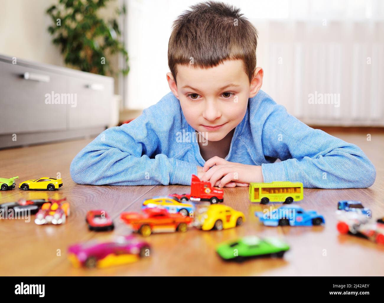 small child preschool boy playing toy cars on the wooden floor in a ...