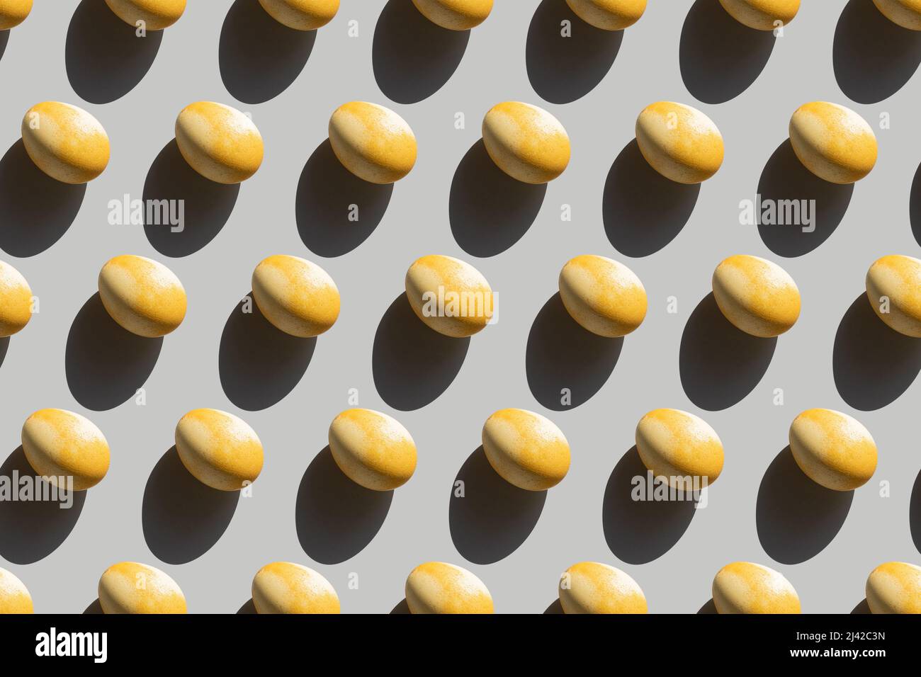 Repeating painted yellow eggs with a hard shadow on a gray background, Easter background in pop art style, seamless pattern with Easter eggs, Stock Photo