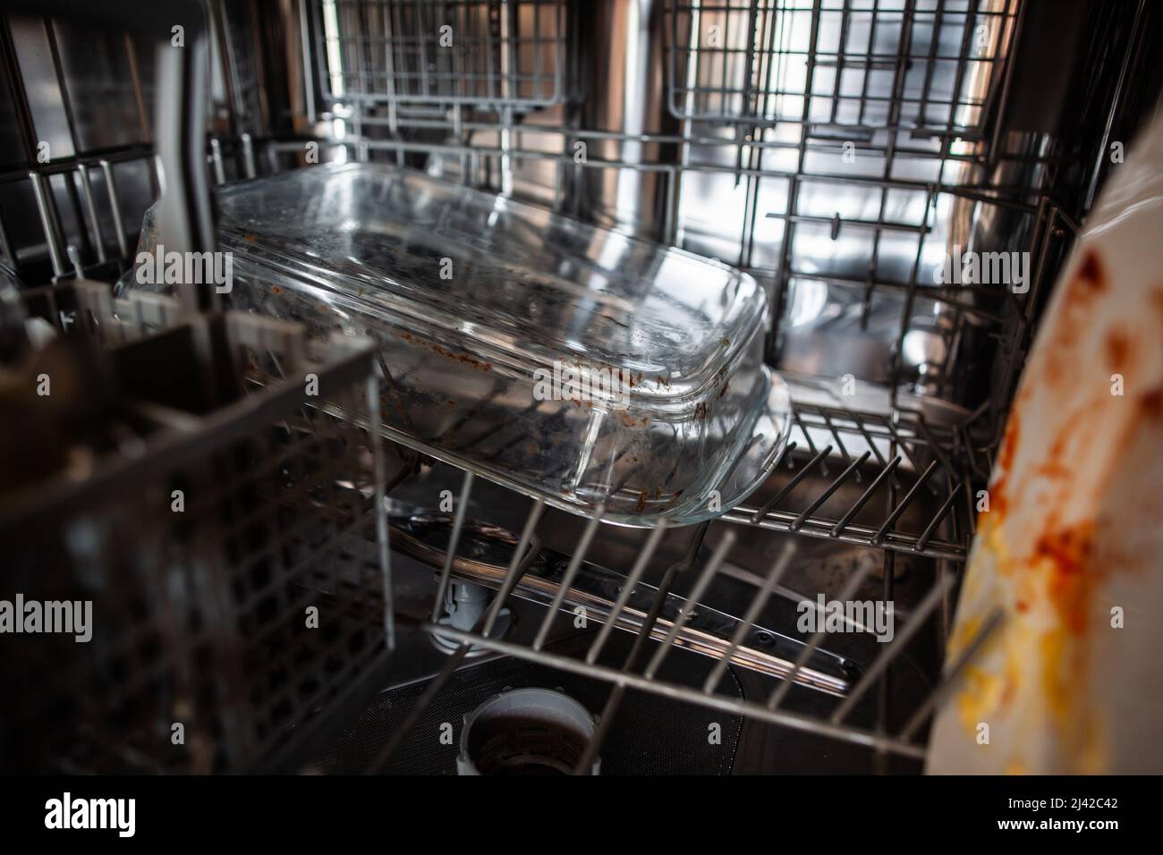 Close up dirty glass casserole dish on bottom rack in dishwasher loaded
