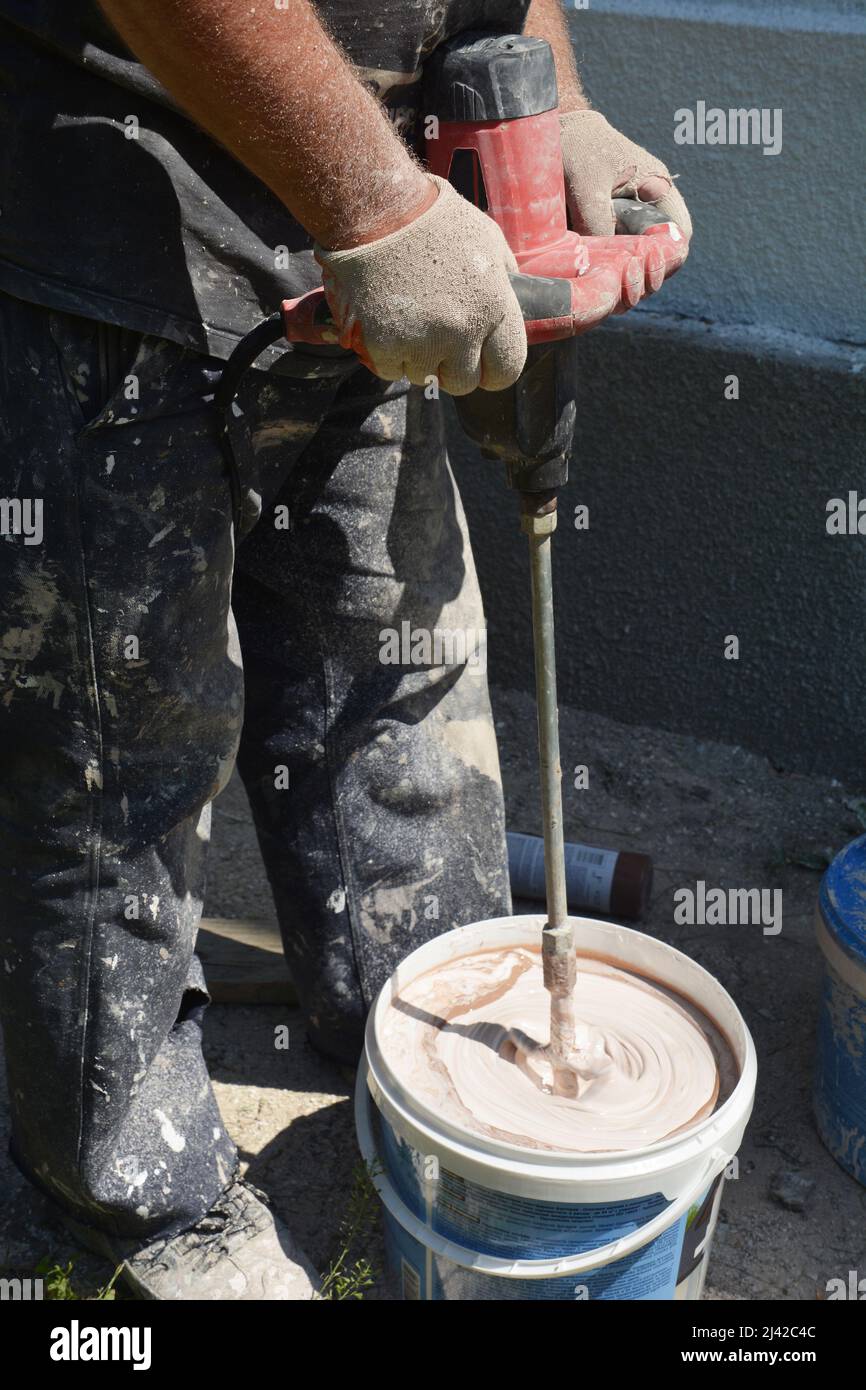 A building contractor is making a stucco finish mix in a bucket using a
