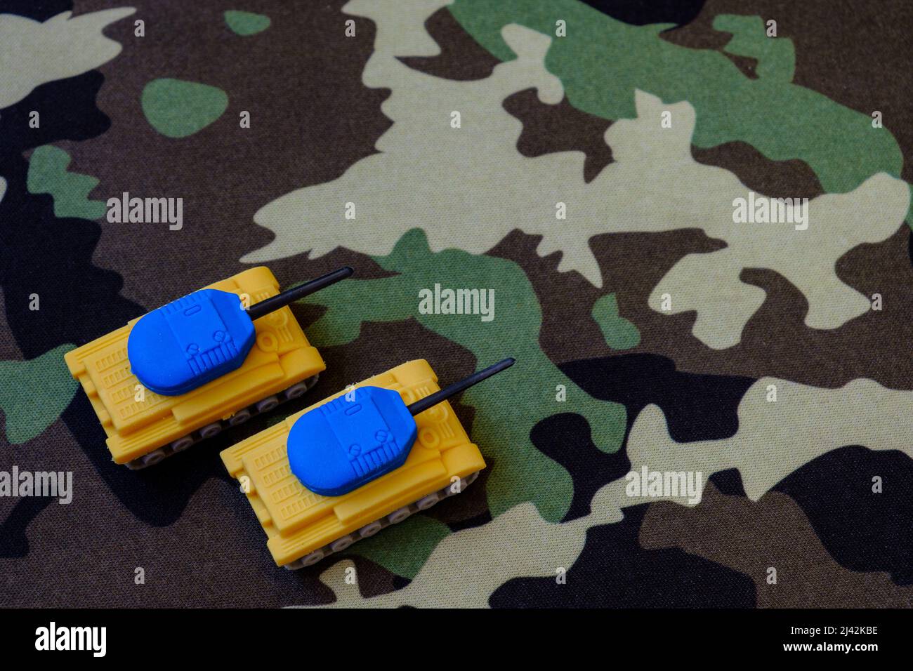 Yellow-blue tanks figures on camouflage background, Ukrainian flag colors on toy tank figures, anti-war concept, selective focus Stock Photo