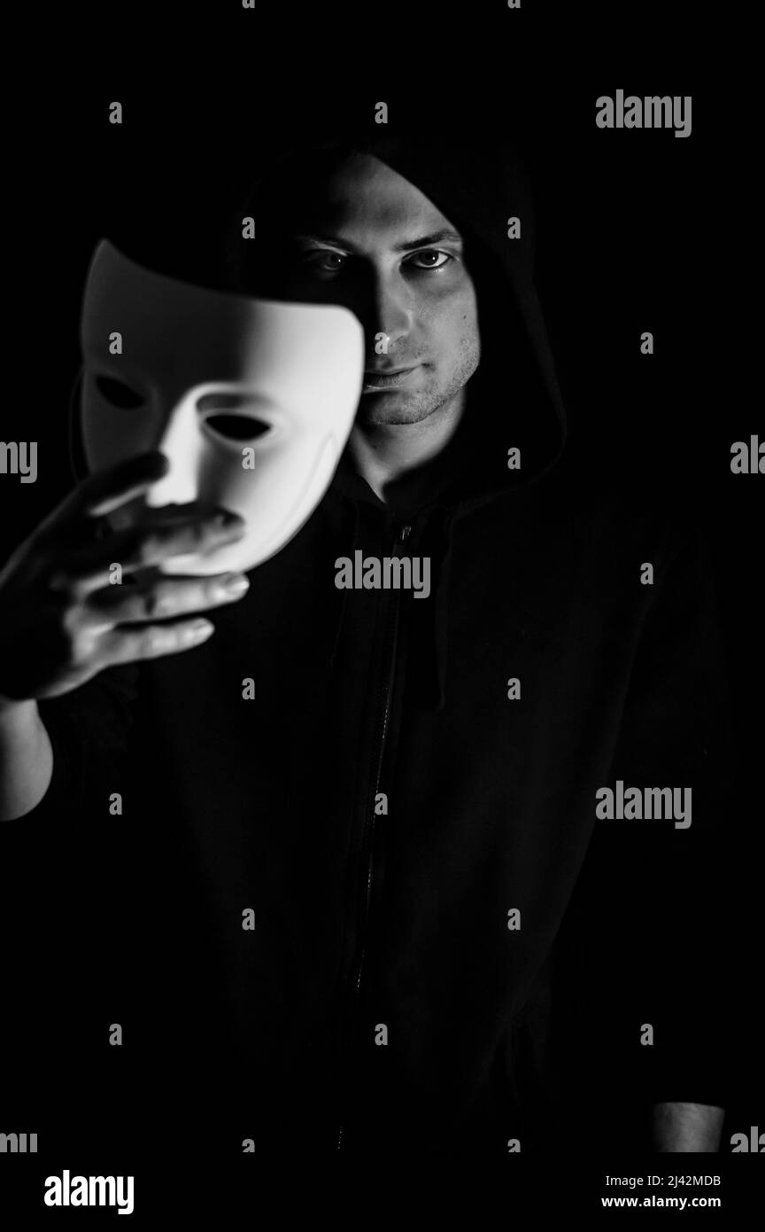 Black and white portrait of a young hooded man taking off his mask, concept for being true and authentic Stock Photo