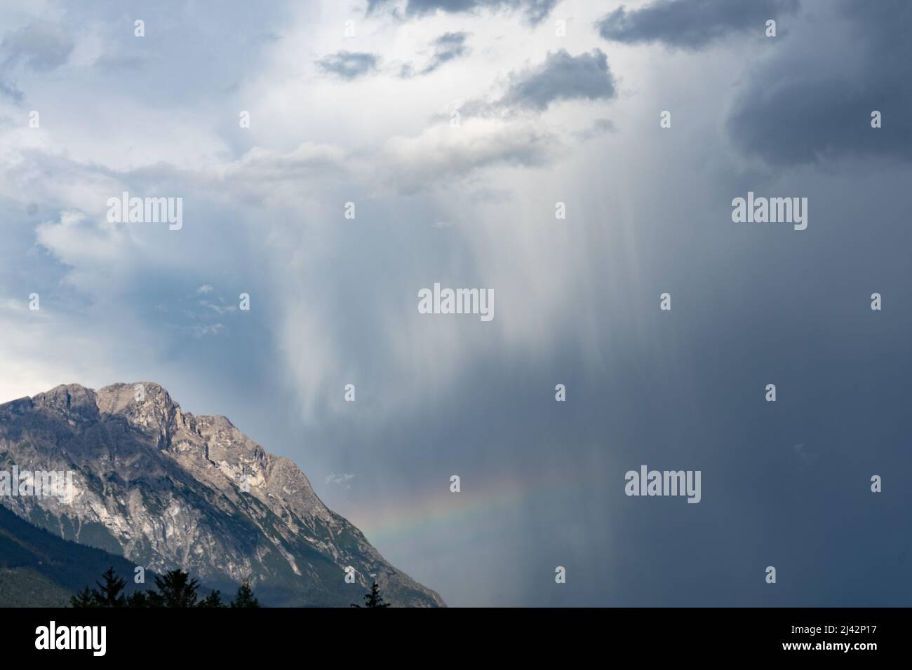 A rainbow forms over a mountain flank after a heavy thunderstorm Stock Photo