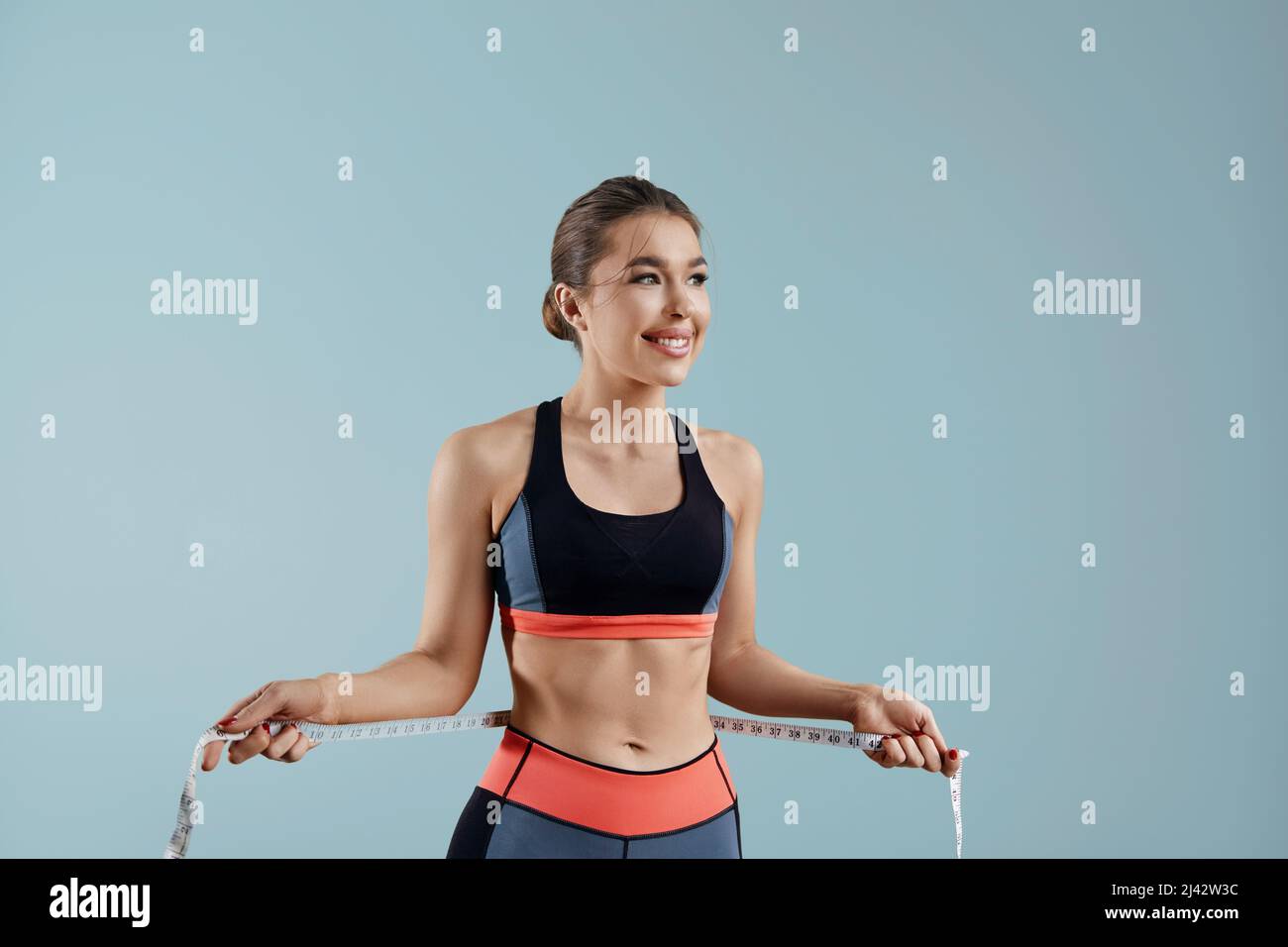 Weight loss, slim body, healthy lifestyle concept. Fit fitness girl measuring her waistline with measure tape. Stock Photo
