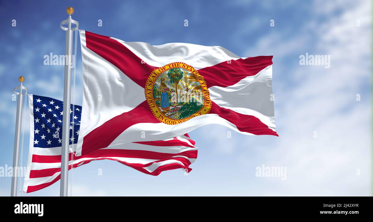 The Florida state flag waving along with the national flag of the United States of America. In the background there is a clear sky. Stock Photo
