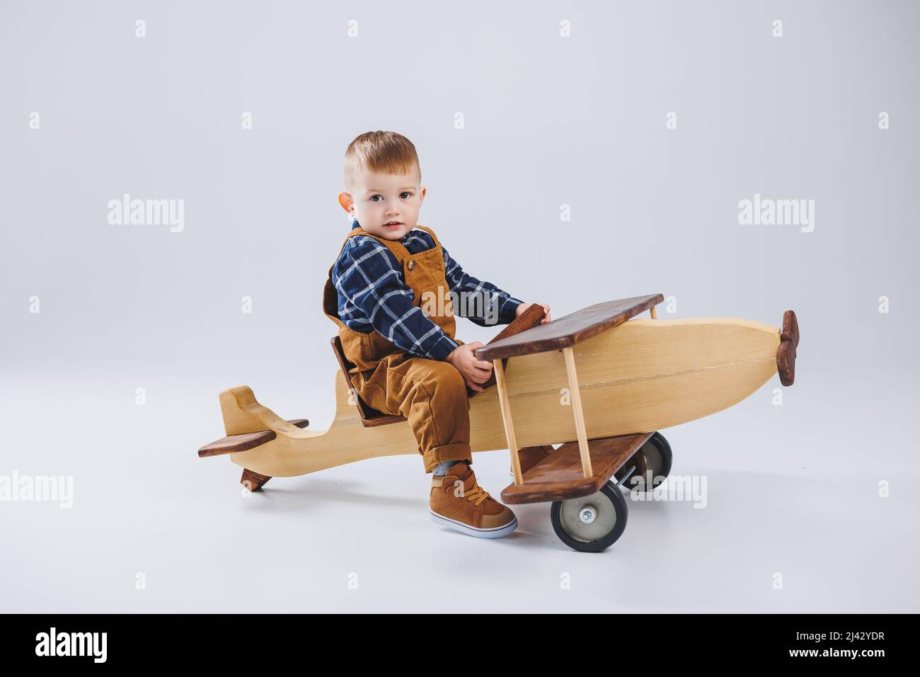 A 3 year old boy in a checkered shirt sits on a large wooden plane