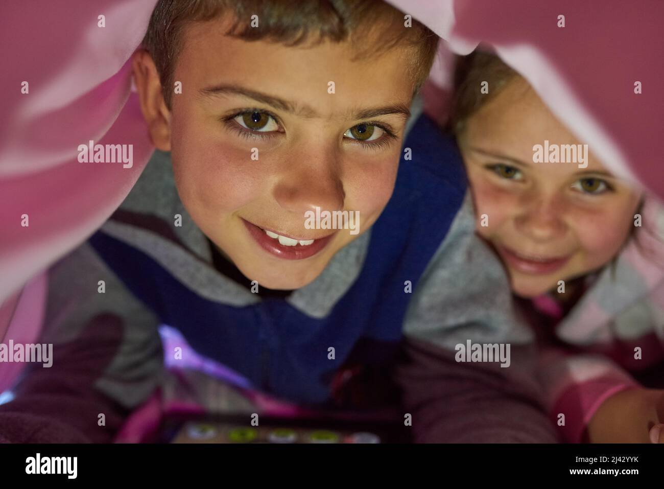 Kids will be kids. Portrait of two young siblings lying down under a blanket at home. Stock Photo