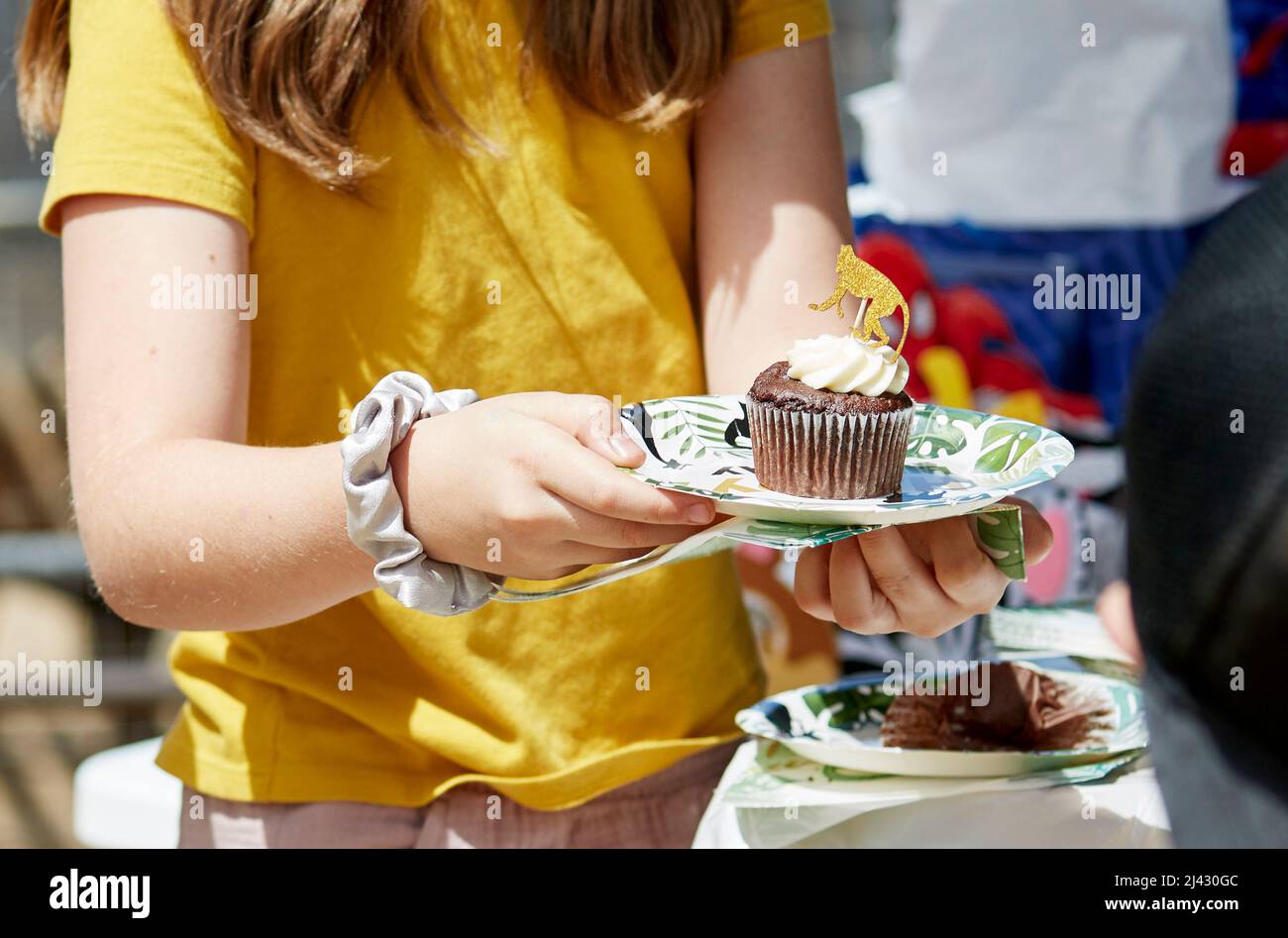 Young Girl holding a paper plate with a cupcake on it at a birthday party Stock Photo