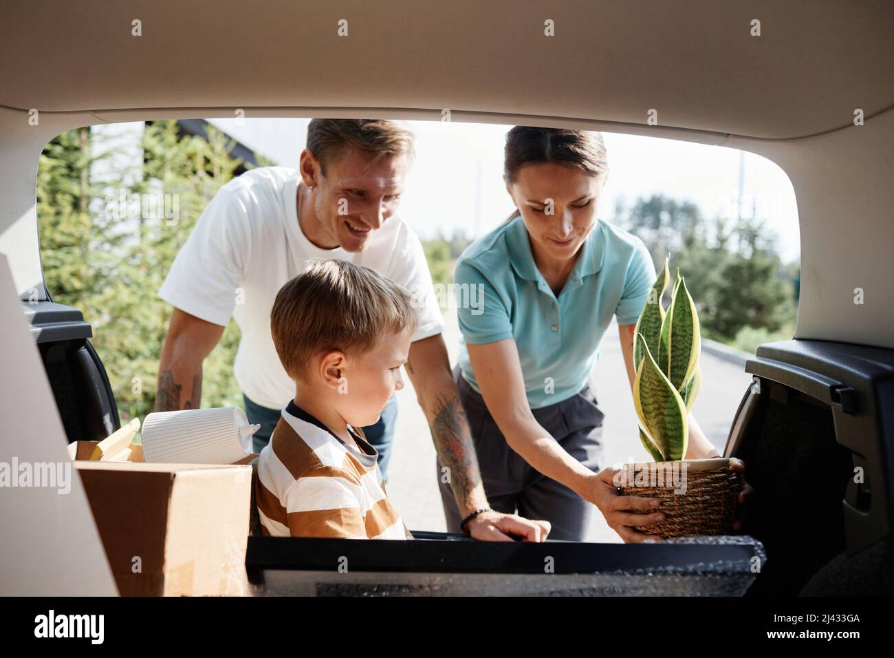 Portrait of smiling family loading boxes in car trunk while moving into new house in sunlight Stock Photo