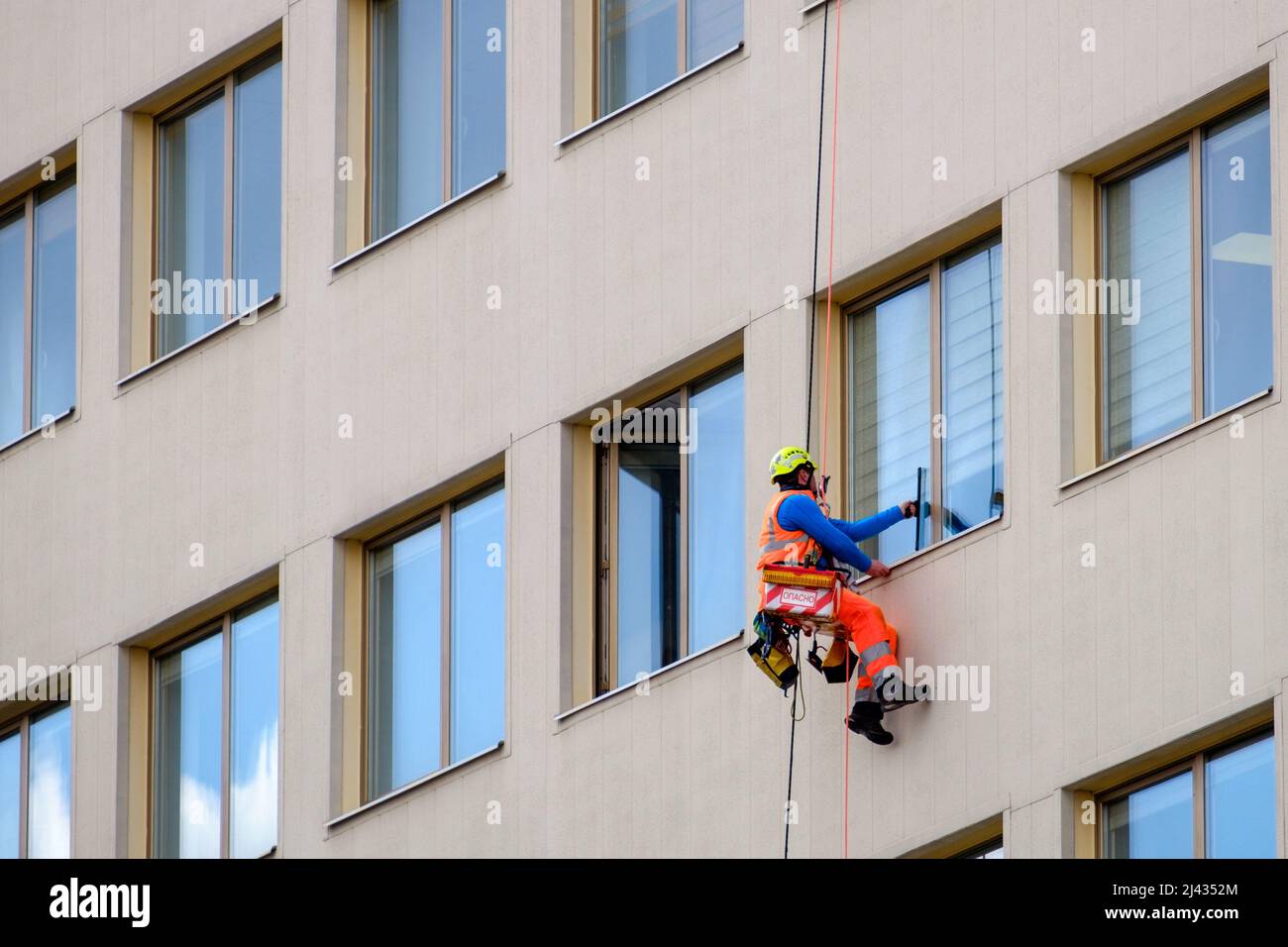Minsk, Belarus - April 11, 2022: Industrial climber washes windows on facade of a building. Side view Stock Photo