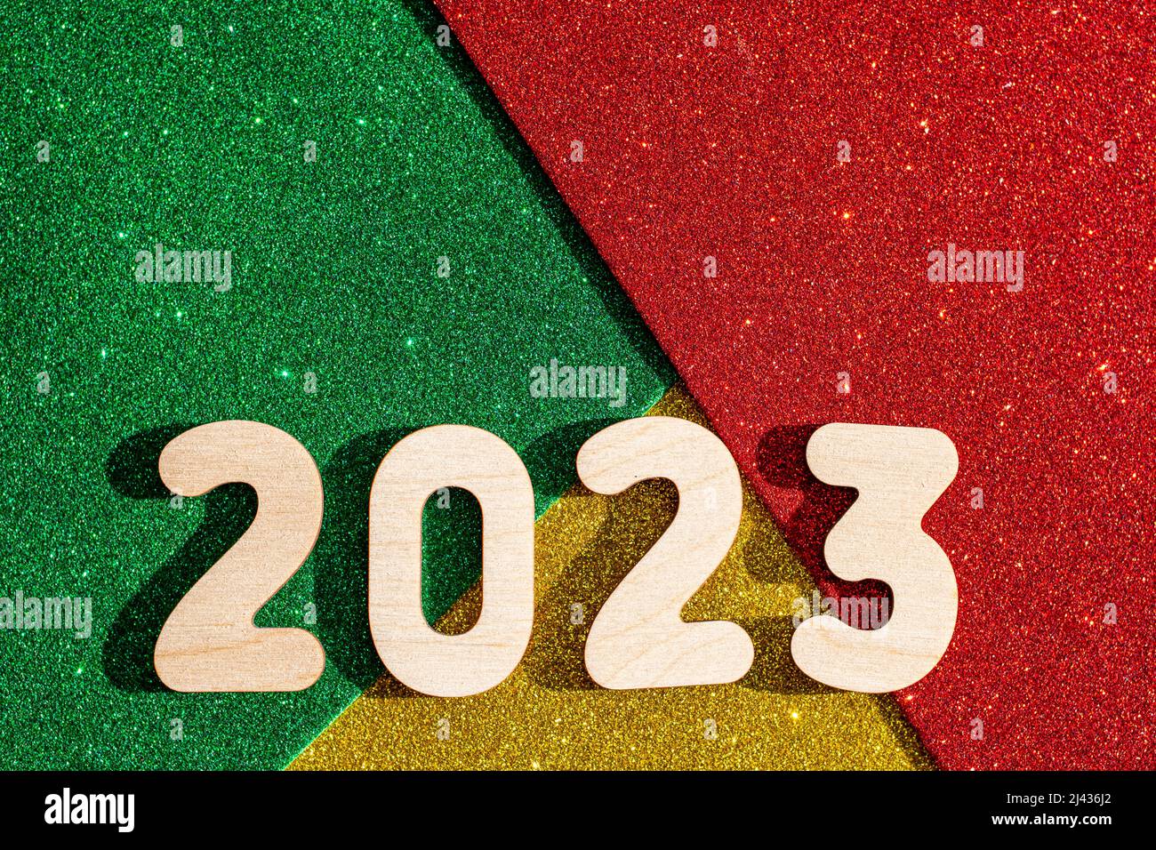 New Years concept - Wooden numbers 2023 on multicolored trending red, green, gold glittering starry background. New Year card. Stock Photo