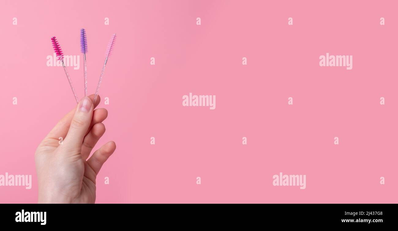 Hand with eyelash wands, brushes on pink background. Banner with copy space for text. High quality photo Stock Photo