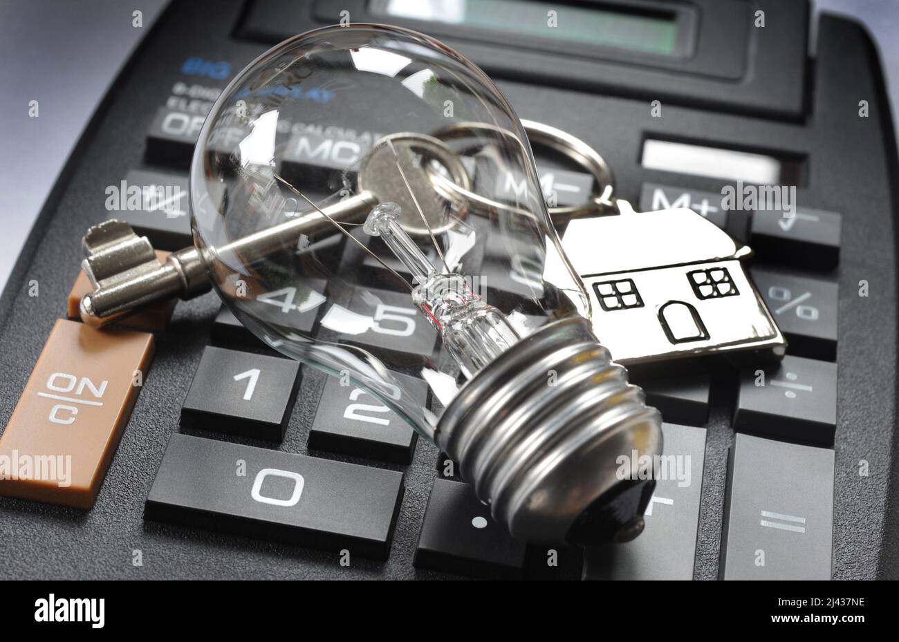 HOUSE KEY AND KEY RING WITH LIGHT BULB ON CALCULATOR RE THE COST OF LIVING ELECTRICITY RISING PRICES HOUSEHOLD  BILLS ELECTRIC UK Stock Photo
