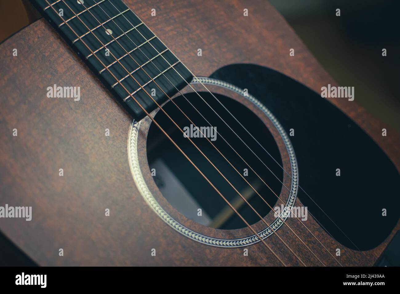A high angle view of the body of an acoustic guitar with the pickguard, sound hole, steel strings and fretboard visible. Stock Photo