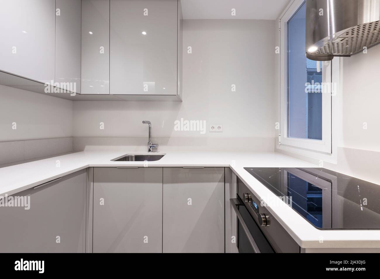 Kitchen with gloss gray wooden furniture combined with white stone countertop, ceramic hob and