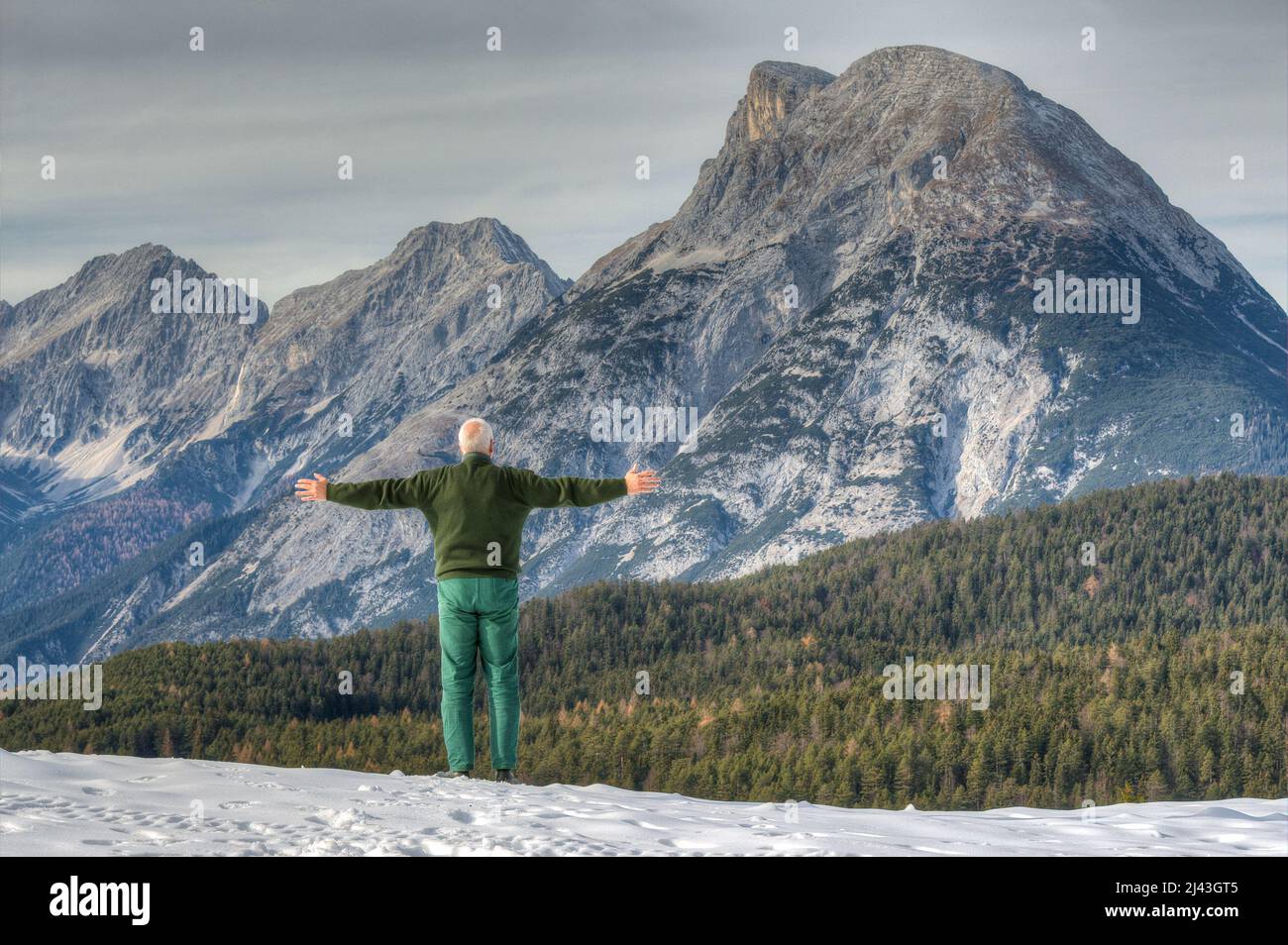 A mountaineer stands in front of the impressive backdrop of the Mount Hohe Munde and would like to embrace this mountain with its unusual shape. Stock Photo