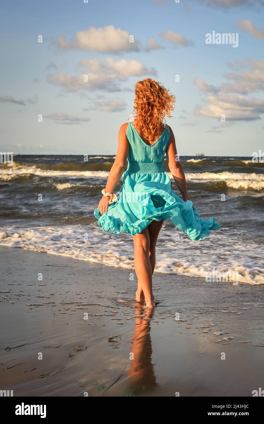 Beautiful blonde haired woman on the beach. Girl in a blue dress at the Polish seaside. Stock Photo