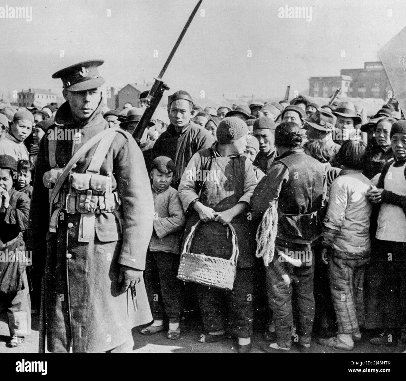 Under The Protection Of 'Tommy' -- Photo just received shows a British tommy on Keswick Road, Shanghai, disciplining the queue of between fifteen and twenty thousand Chinese who cross daily into the conquered areas for firewood and food, and return by four p.m. (Japanese curfow). March 21, 1938. (Photo by London News Agency Photos Ltd.). Stock Photo
