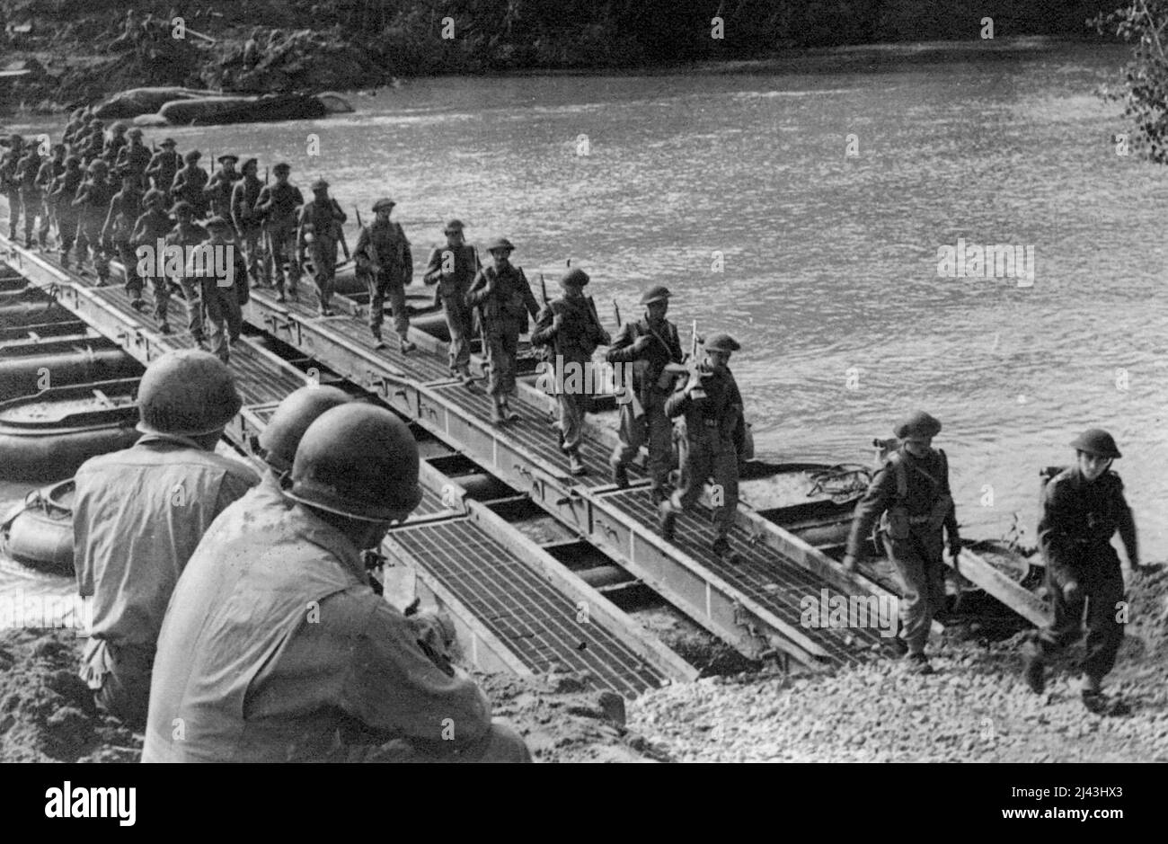 Crossing the River Volturno: Three American engineers watch British troops and transport crossing a Volturno Bridge. On October 13th, 1943, under cover of darkness the Fifth Army made its big assault on the River Volturno, one of the major barriers to advance on Rome - and crossed in force. October 31, 1943. (Photo by Fox Photos). Stock Photo