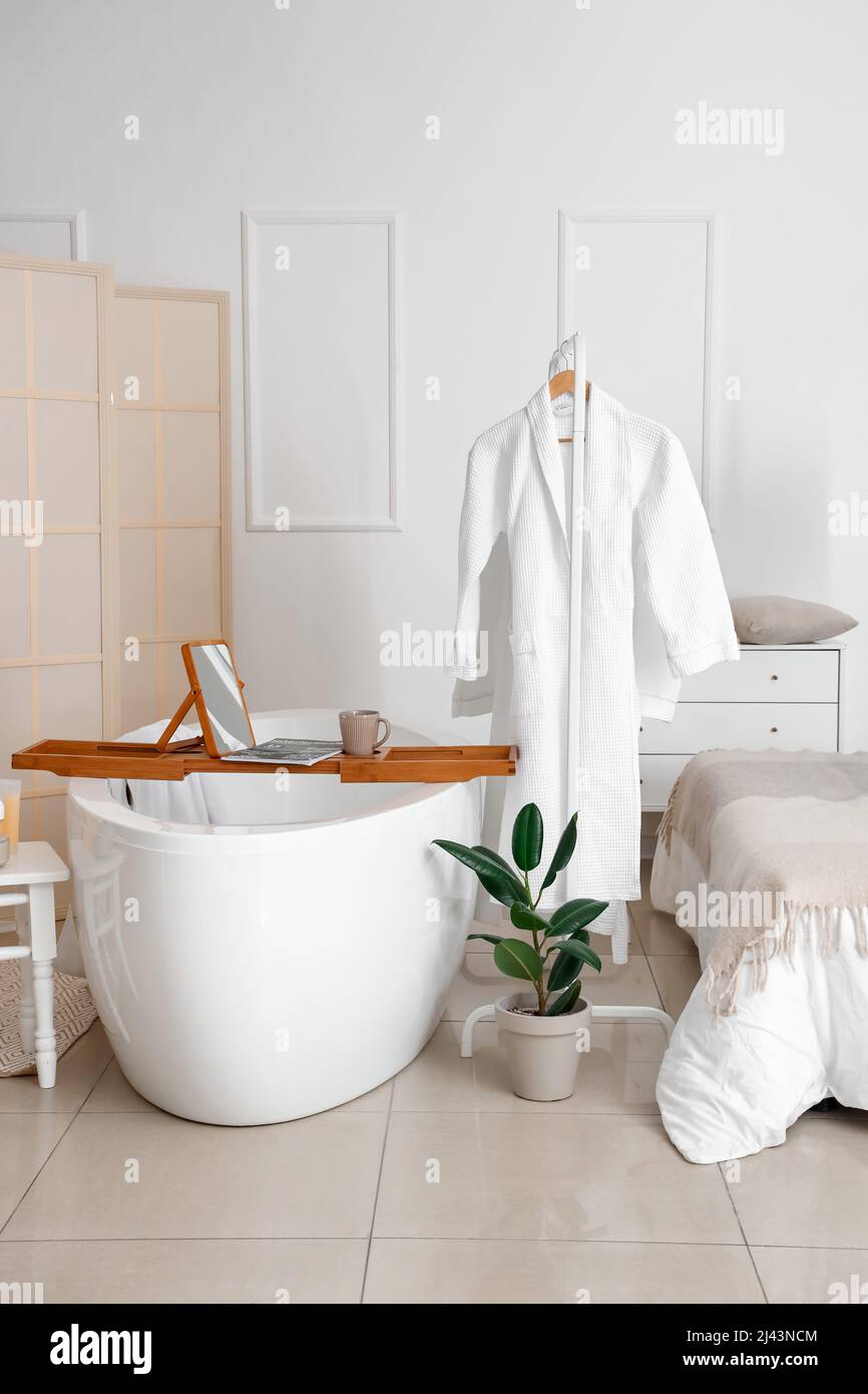 Interior of modern bedroom with bathtub, rack and bathrobes Stock Photo ...