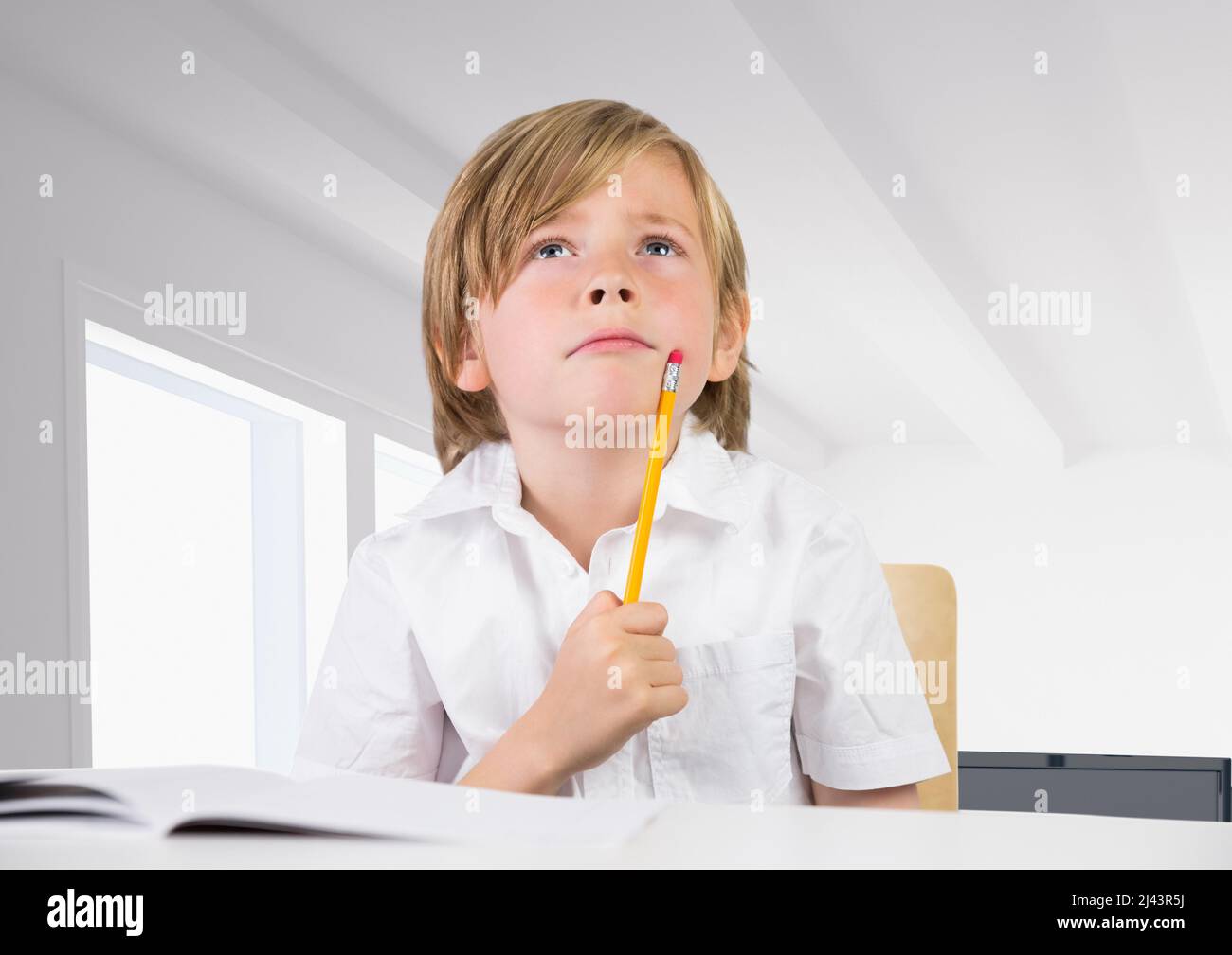 Thoughtful caucasian boy holding a pencil at school against office in background Stock Photo