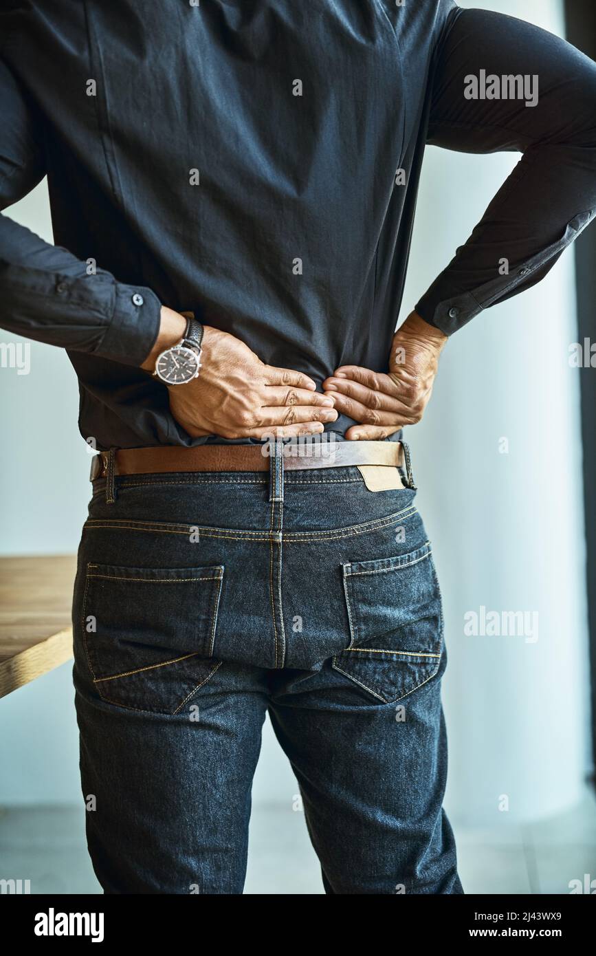 His back muscles are getting tense and tight. Shot of a young businessman suffering from back pain while working in an office. Stock Photo