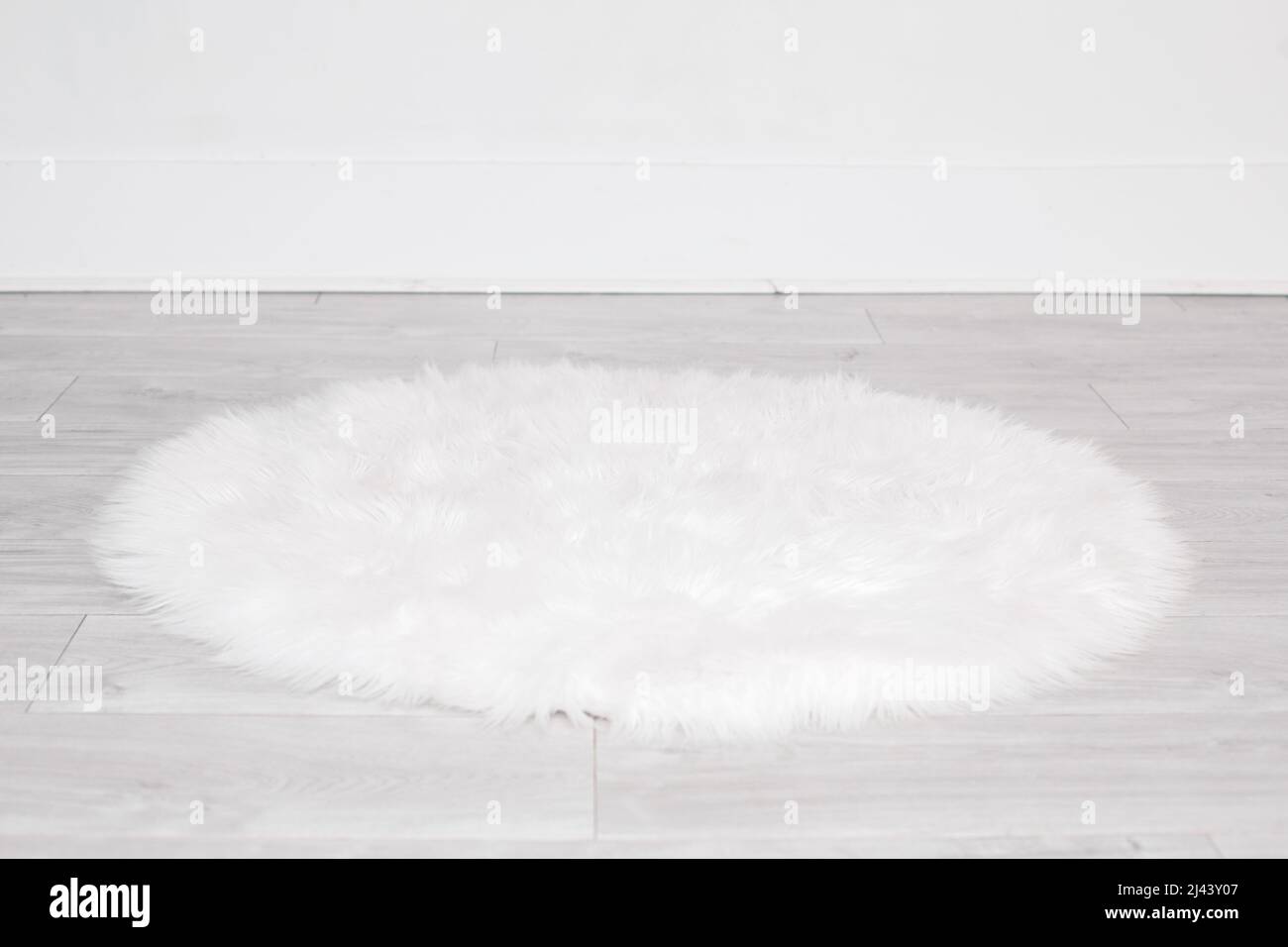 White round fluffy rug carpet lying on floor by white wall at home. Background mockup for designs and backdrop. Stock Photo