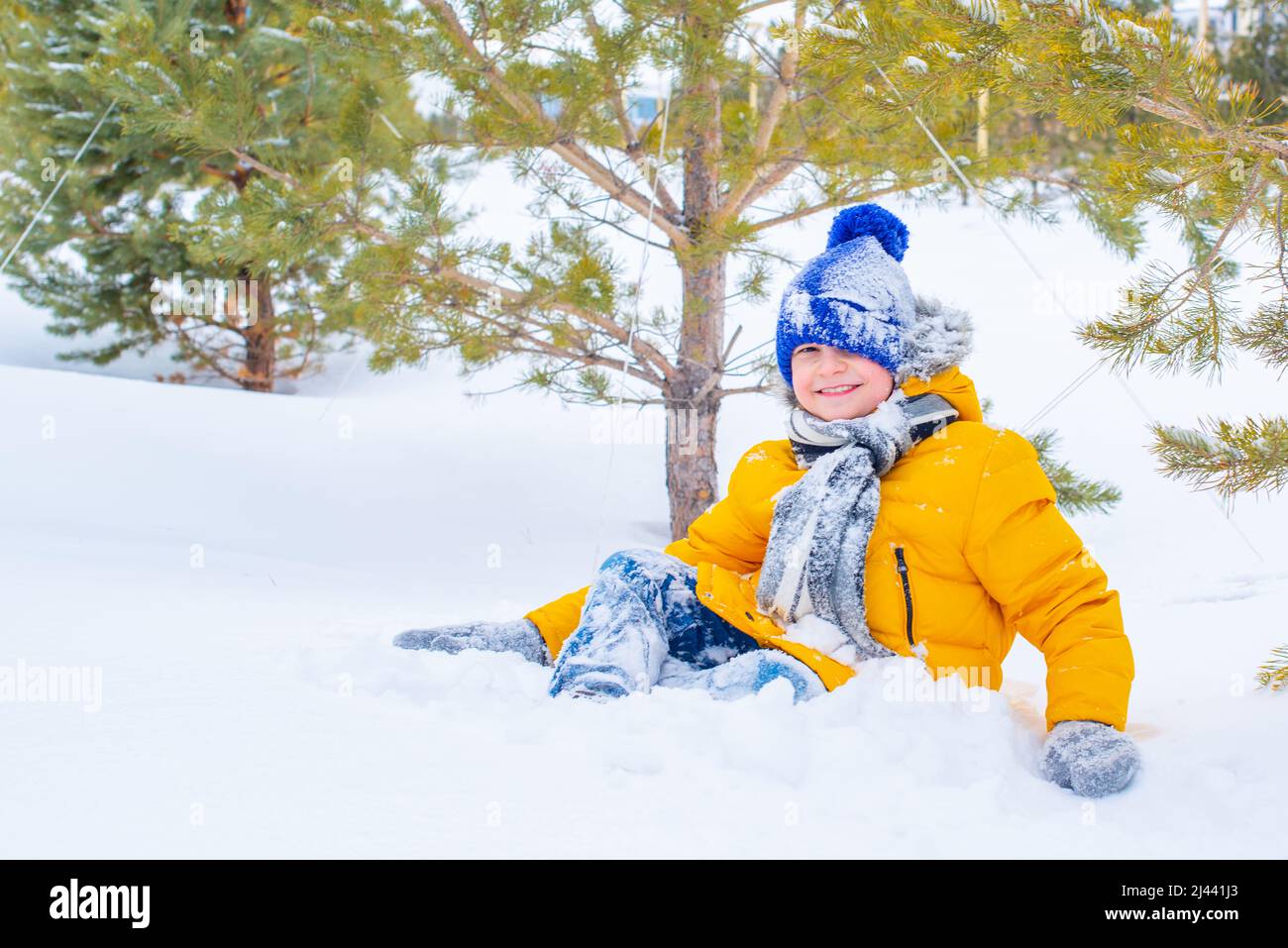 cheerful boy playing snowballs in a yellow jacket and a blue hat Stock Photo