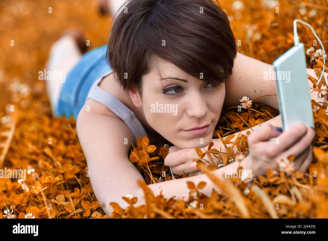Young woman listening to music or watching media on a mobile phone as she relaxes in a meadow amongst the wildflowers Stock Photo