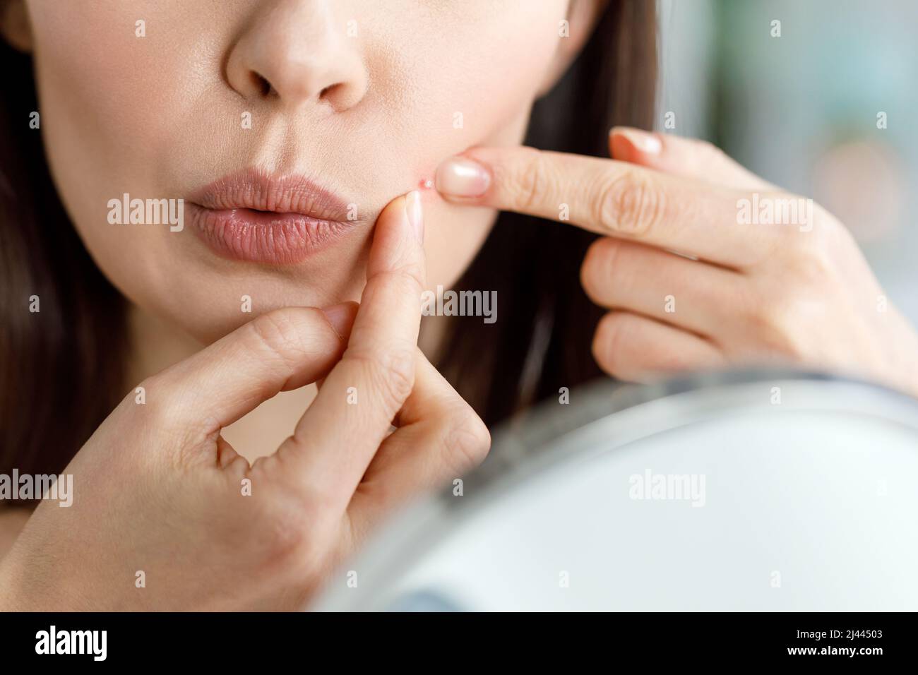 A woman crushes a pimple while looking in the mirror. Stock Photo