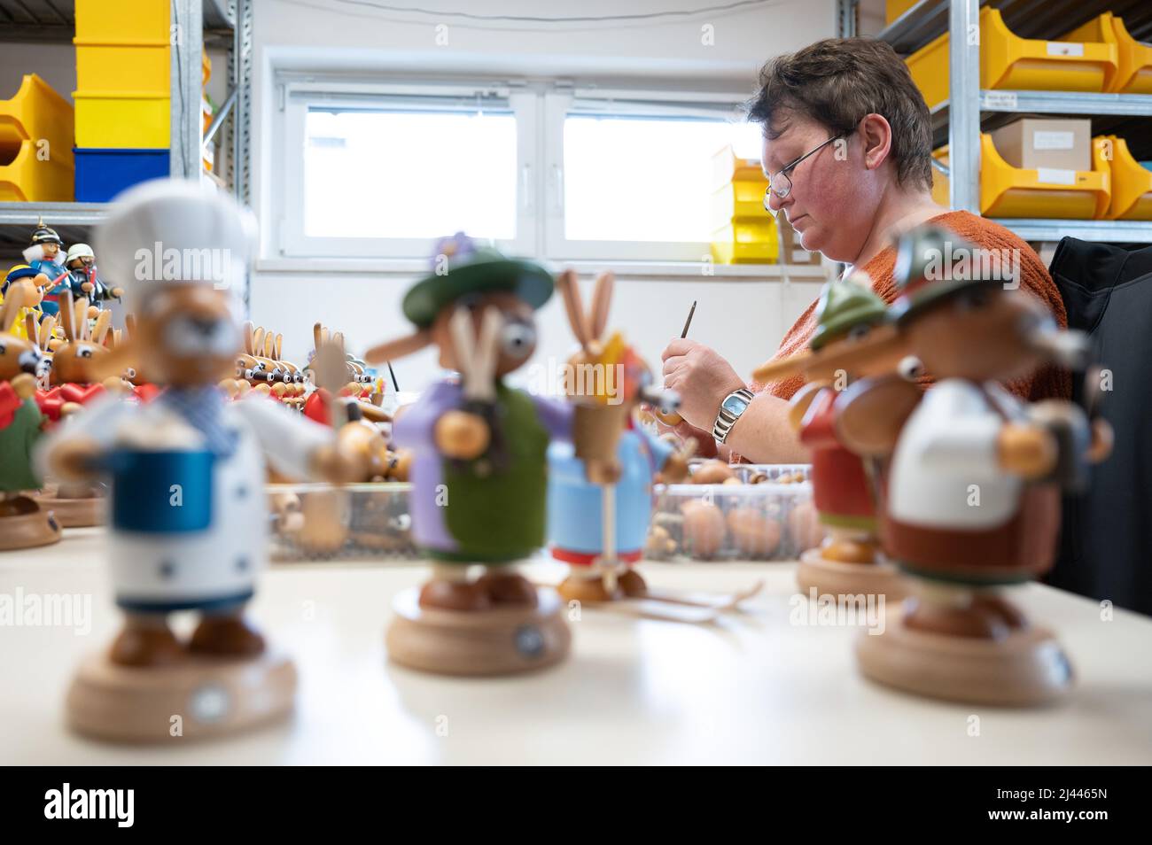 06 April 2022, Saxony, Seiffen: Jana Frank, wooden toy maker, sits behind numerous smoked bunnies in production at the Müller wood art manufactory. The master wood toy maker Ringo Müller from Seiffen has taught the Easter bunny to smoke. Not only at Christmas do candle arches, pyramids and incense smokers from the Erzgebirge decorate houses and living rooms in many places. Also around spring and Easter, the craftsmen from the Erzgebirge demonstrate their creativity. (to dpa 'Smoking bunnies and flower children: arts and crafts provide Easter decorations') Photo: Sebastian Kahnert/dpa Stock Photo