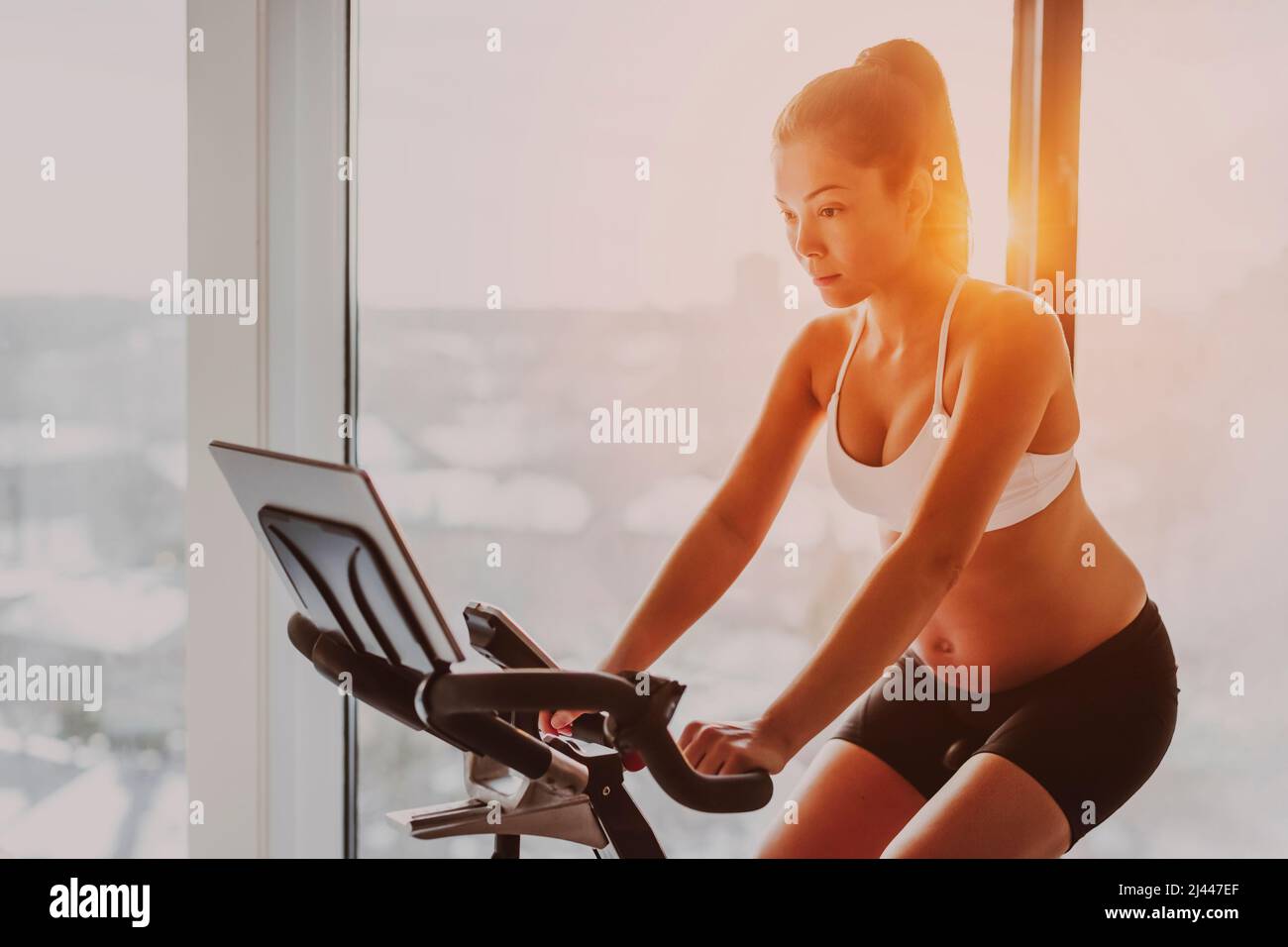 Exercise bike Asian woman training during pregnancy. Workout at home fitness gym watching online cycle class on stationary bicycle Stock Photo