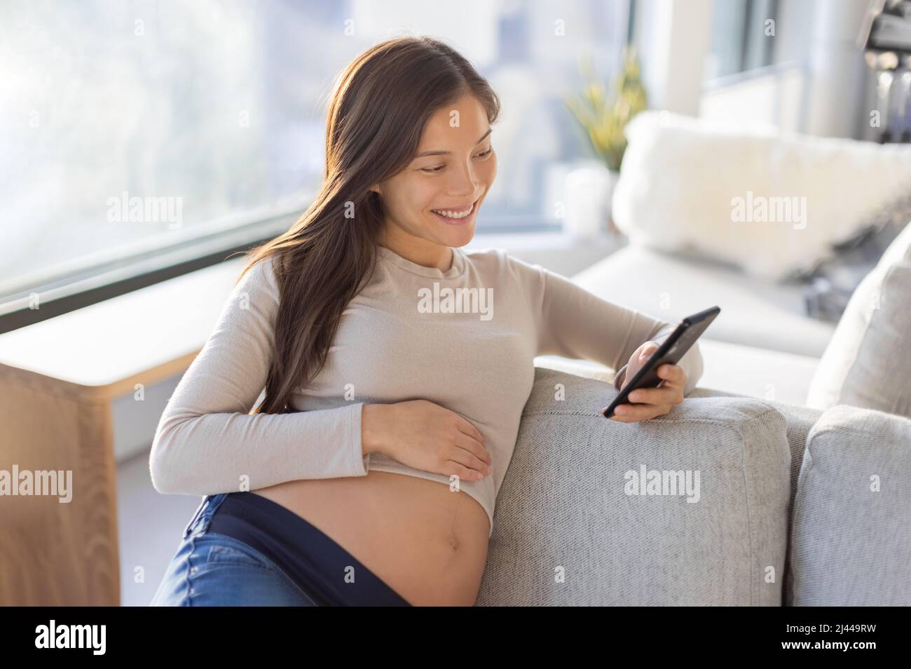 Pregnant Asian woman happy using mobile phone app for shopping or telemedicine. Pregnancy lifestyle at home Stock Photo