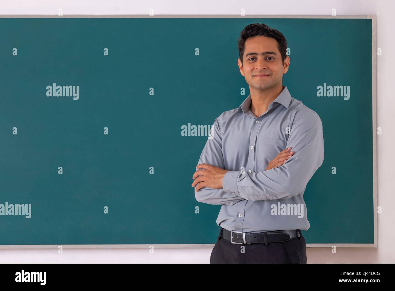 School teacher standing in front of blackboard with arms folded in classroom Stock Photo