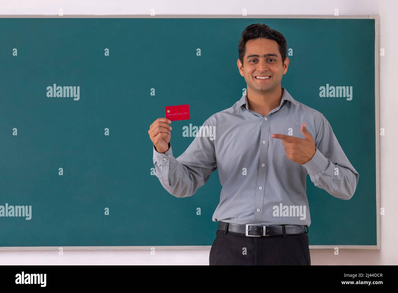 School teacher pointing at credit card while standing in front of blackboard in classroom Stock Photo