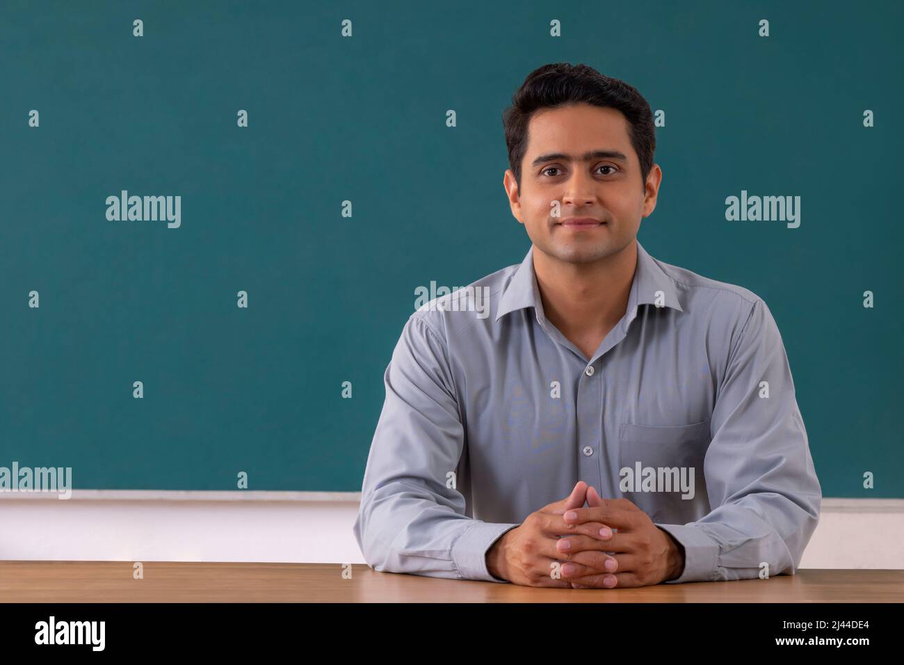 School teacher sitting in front of blackboard in classroom Stock Photo