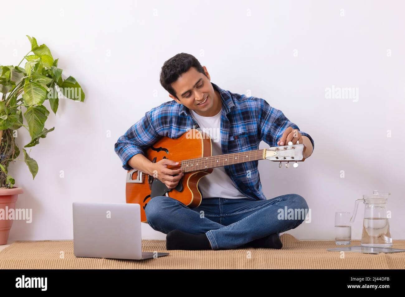 Young music teacher tuning guitar during online class in living room Stock Photo