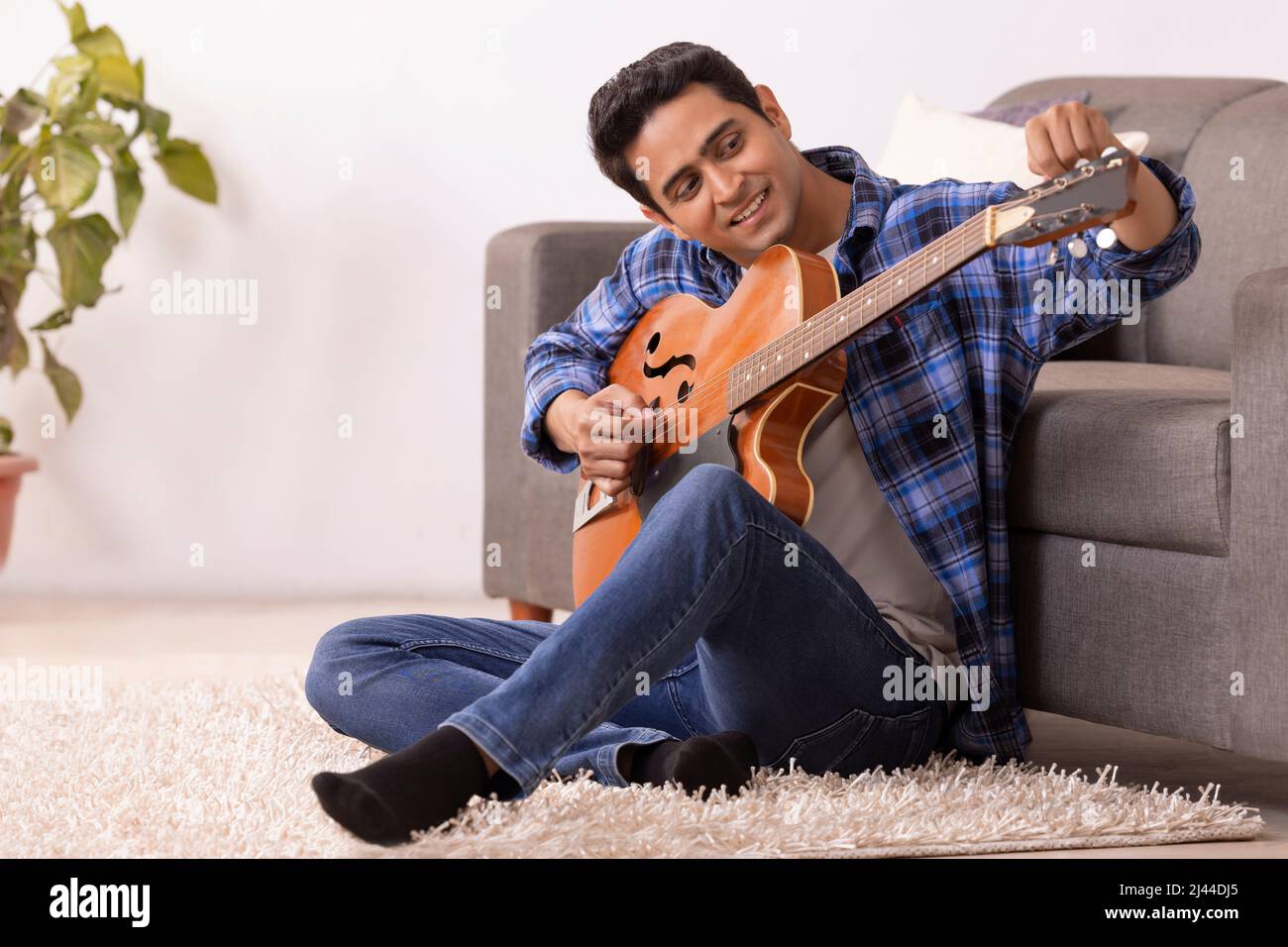 Portrait of a young musician tuning guitar in living room Stock Photo