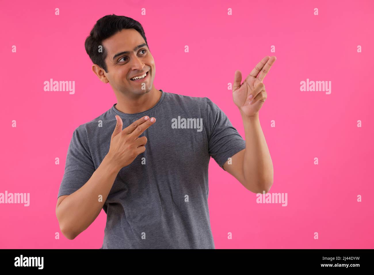 Portrait of a young man pointing away with fingers against pink background Stock Photo