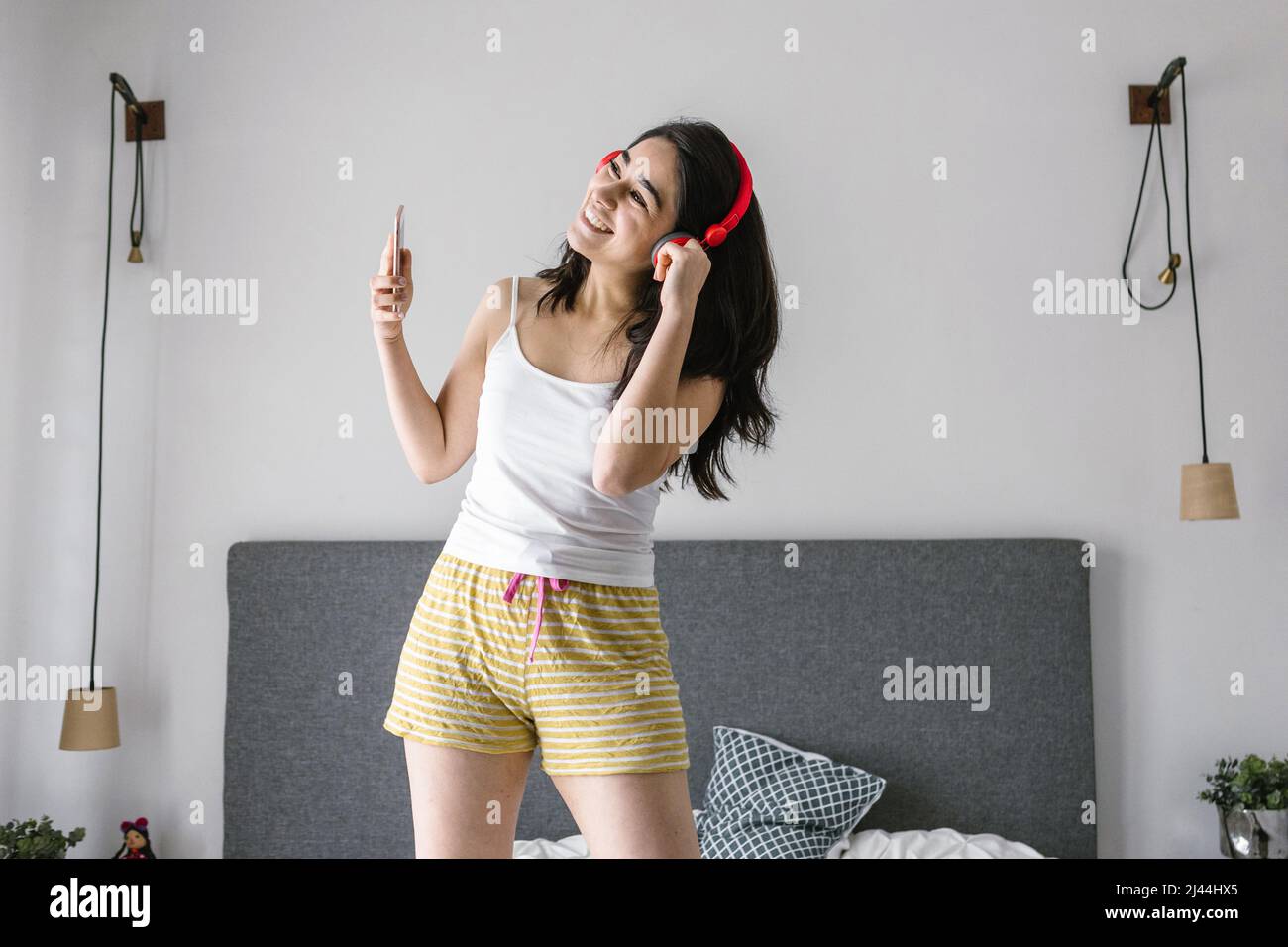 Young latin woman listening music with headphones on bed at home in Mexico Latin America Stock Photo