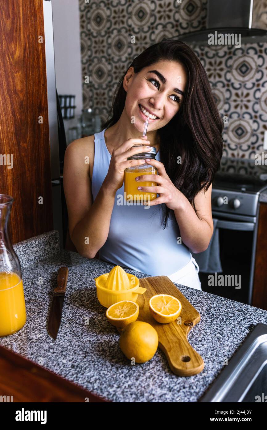 Hispanic young latin woman preparing orange juice at the kitchen in
